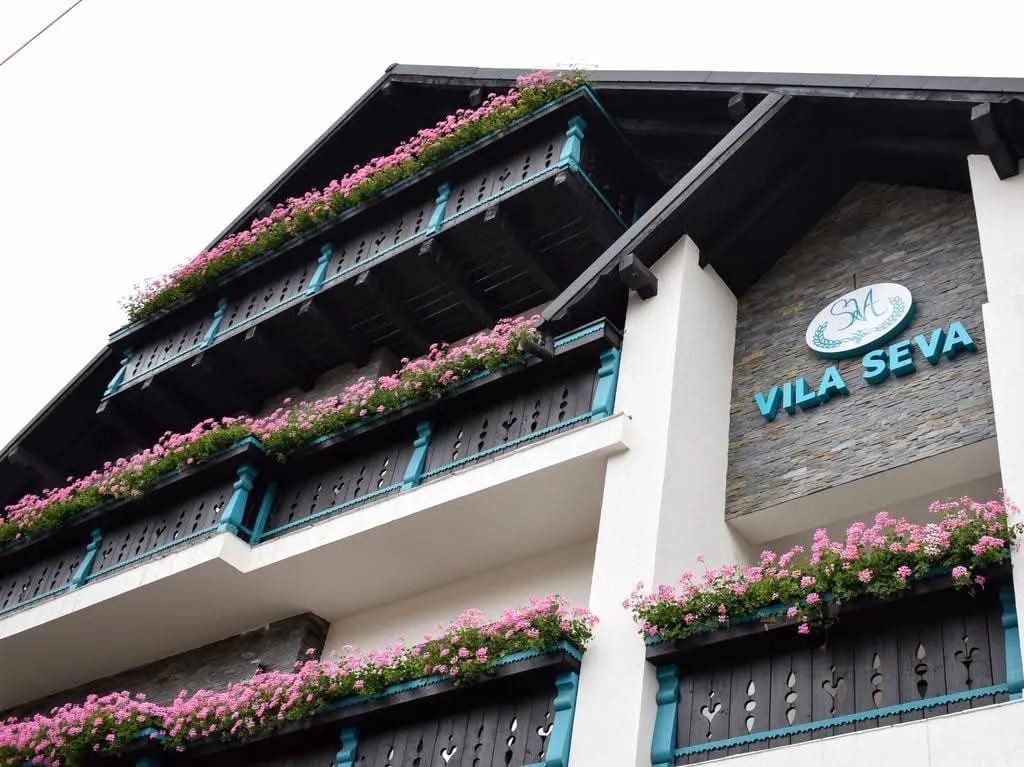 The façade of Vila Seva, with its sign and the balconies with geraniums